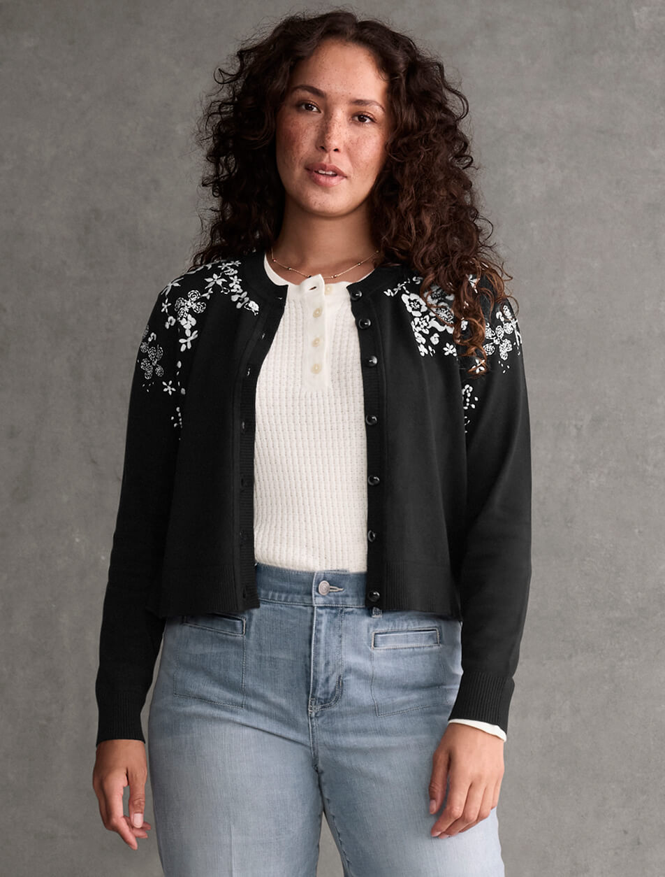 Female model wearing a black cardigan over a white knit top with light wash denim